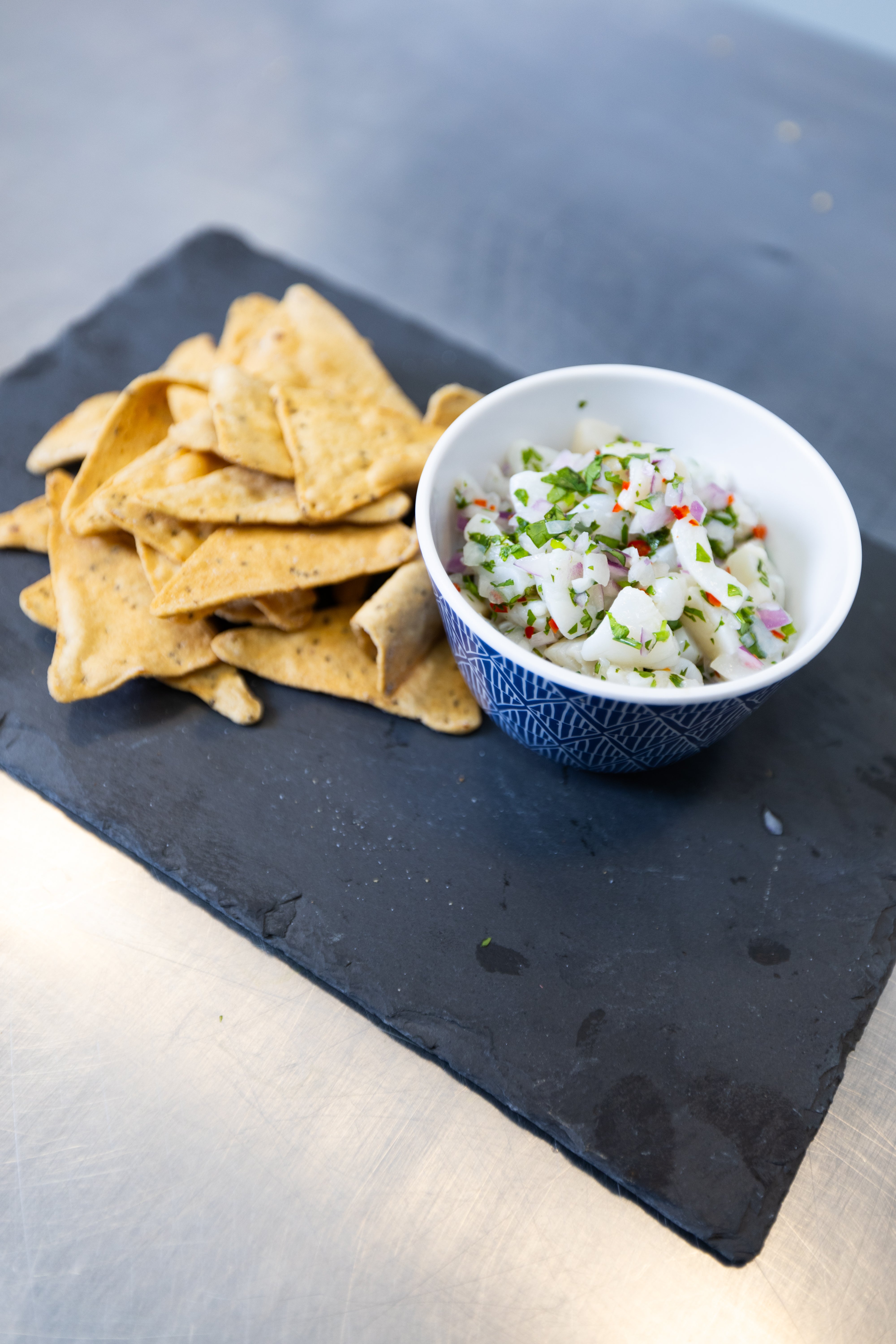 A bowl of fresh scallop salad next to a pile of chips