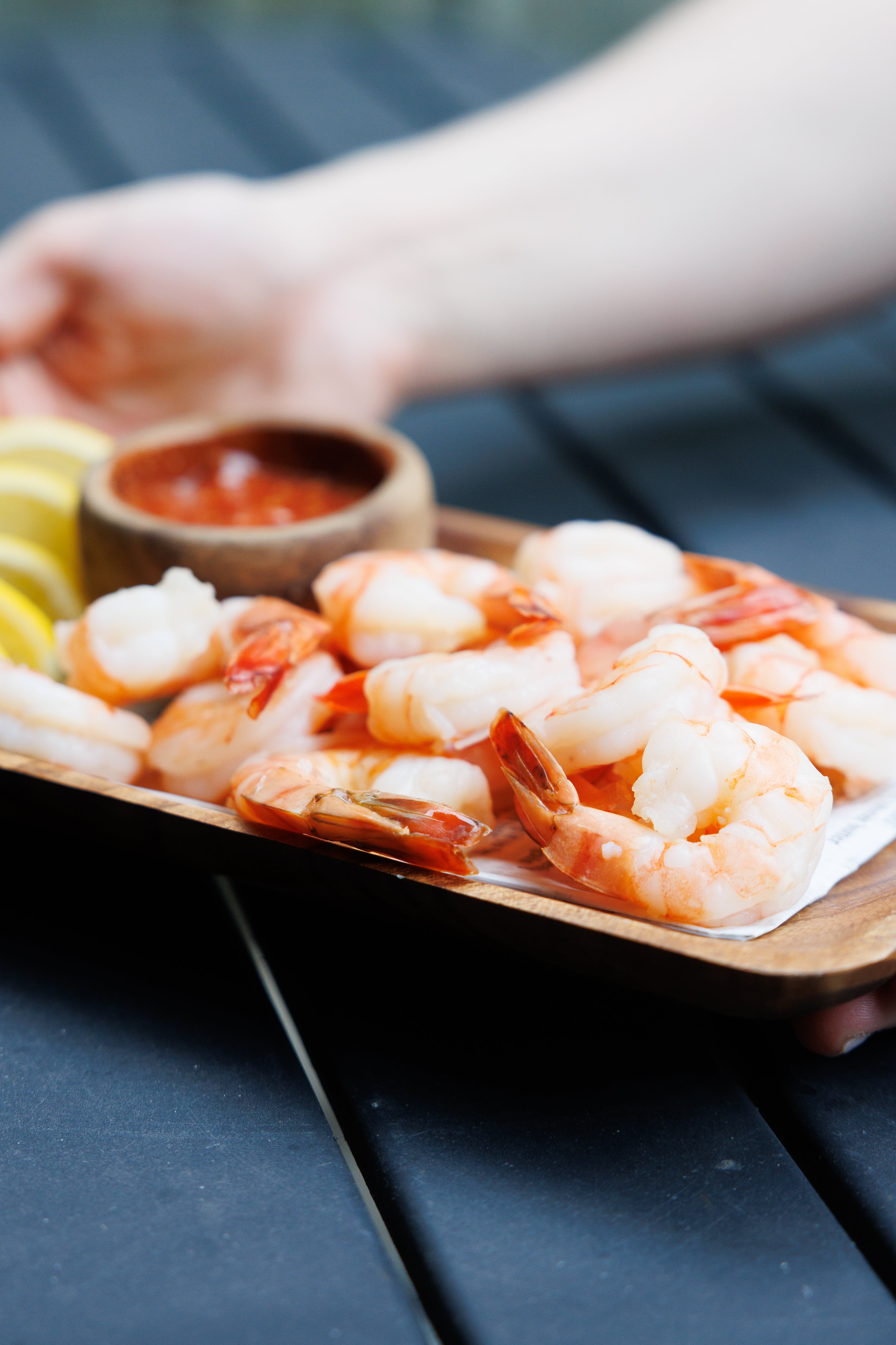 A platter of cooked cocktail shrimp next to a bowl of cocktail sauce