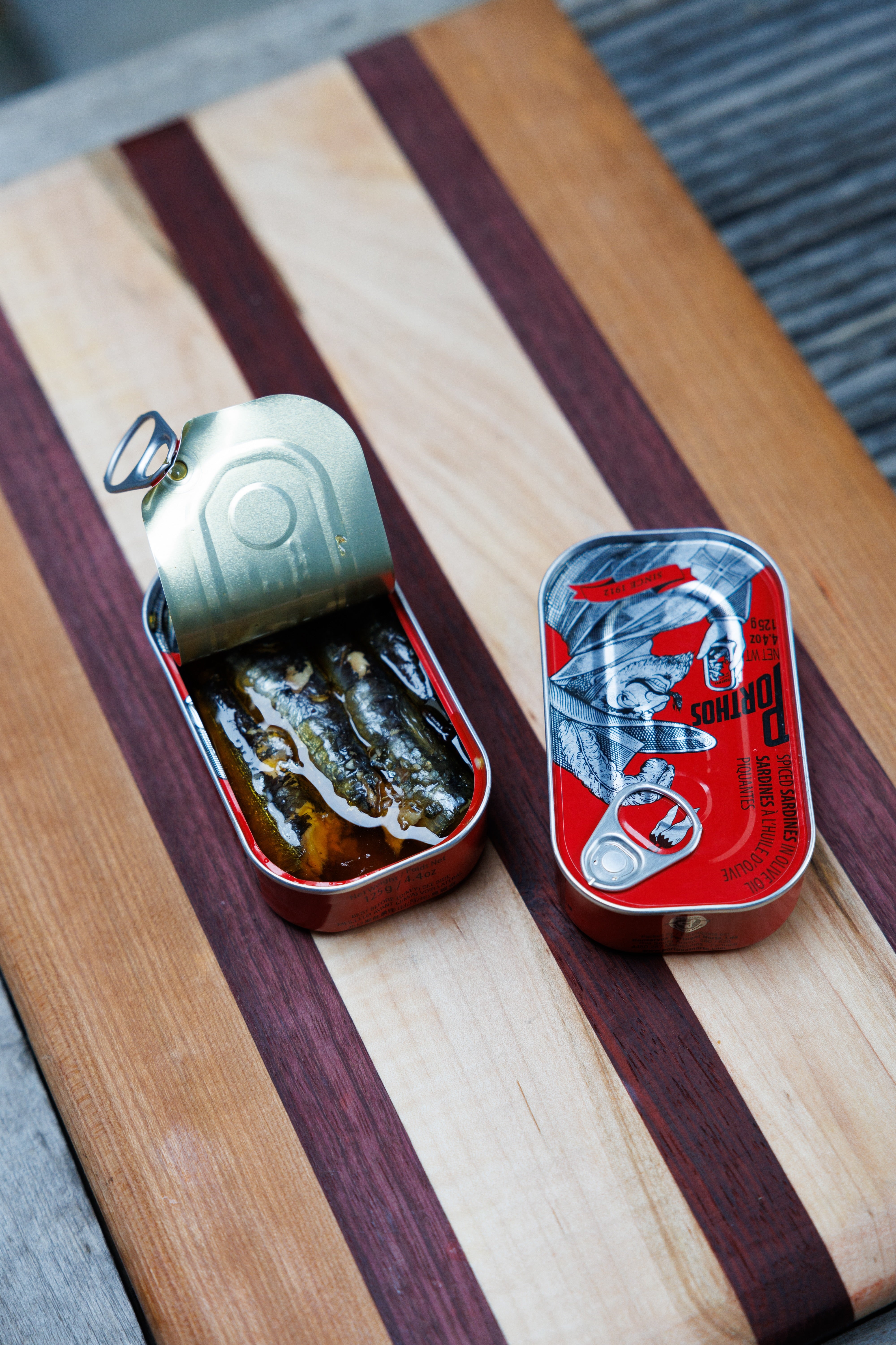 Opened and unopened tins of Porthos Spiced Sardines in Olive Oil