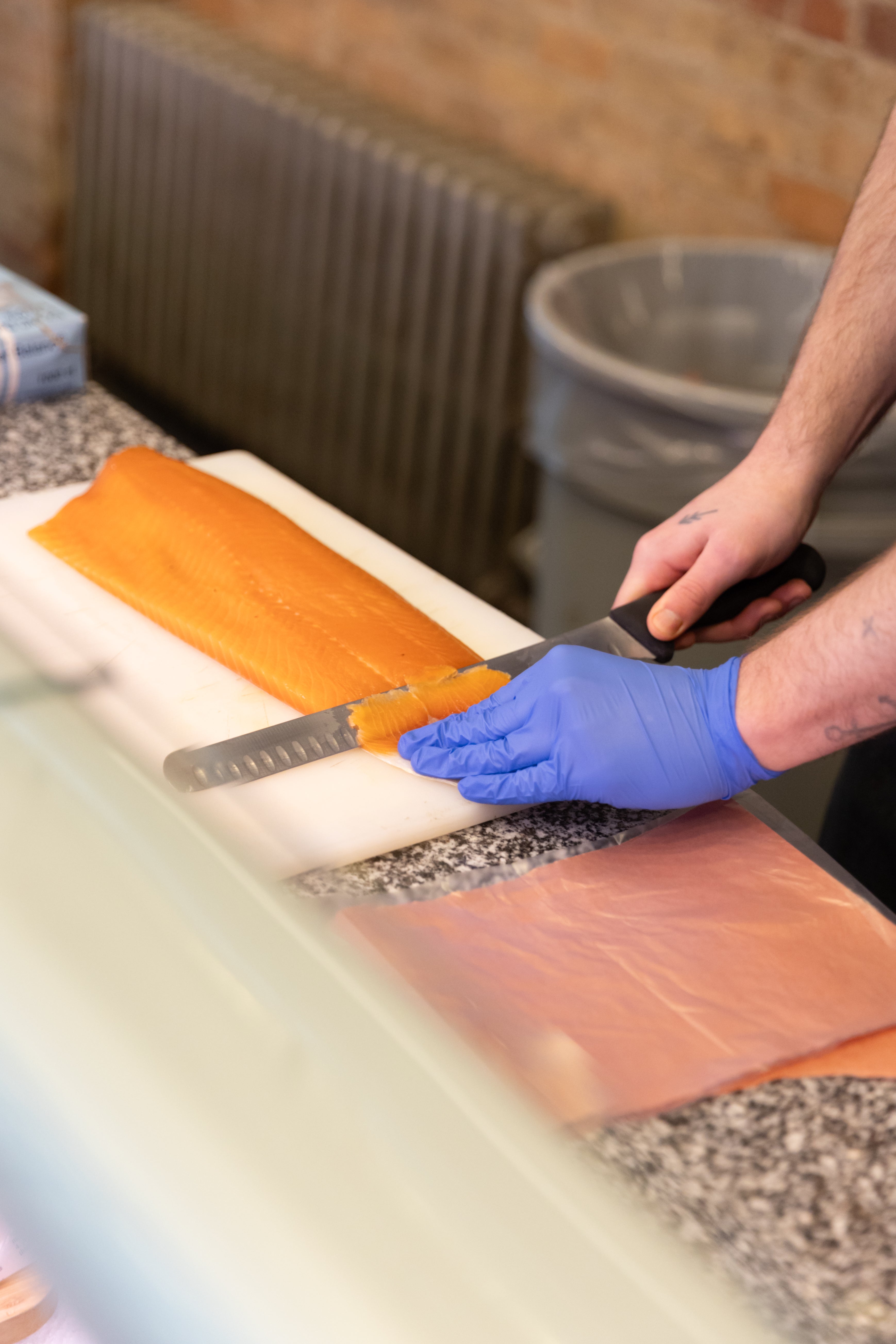 A gloved hand slicing cold smoked salmon with a knife